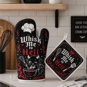 May include: Black oven mitt and pot holder set with a devilish theme. The mitt and pot holder feature the text "Whisk Me to Hell" with a cartoon devil illustration. The pot holder is square with a white border. A black candle with the text "Kitchen Witch" is also visible.