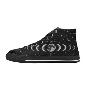 May include: Black high-top canvas sneakers with a celestial design. The sneakers feature a black rubber sole and a white stripe. The upper is decorated with phases of the moon, stars, and bats.