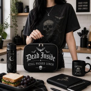 Pu&ograve; includere: Borsa per il pranzo nera con la scritta "Dead Inside Still Packed Lunch" e un design a teschio e pipistrello. Sono visibili anche una borraccia nera, una tazza da caff&egrave; con "Caffeine & Chaos" e un taccuino. Il tema &egrave; gotico.