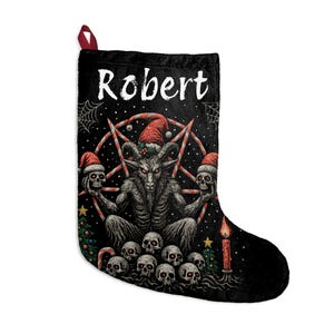 Puede incluir: Calcetín navideño negro con lazo rojo. El calcetín presenta un gráfico de una figura con cuernos con gorro de Papá Noel, sosteniendo calaveras y rodeada de calaveras, un pentagrama y el nombre "Robert".