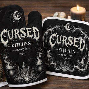 Peut inclure: Ensemble de manique et de manique noirs avec le texte "Cursed Kitchen" dans une police gothique. Le motif comprend un croissant de lune, des cristaux et des chaudrons. Le dessous de plat a une bordure blanche.