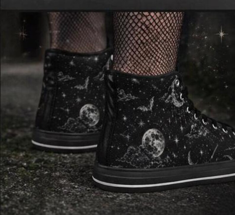 May include: Black high-top sneakers with a celestial design. The sneakers feature a black base with a pattern of moons, stars, and bats. The soles are black with a white stripe.