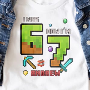 May include: White t-shirt with a pixelated "6" and "7" design, along with the text "I WAS 6 NOW I'M 7 ANDREW". The shirt features a pickaxe, TNT, and a sword. A blue denim jacket is draped over the shirt.