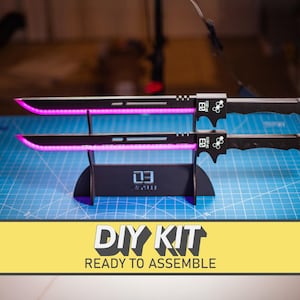 May include: Black DIY kit with two swords, each with a black handle and a glowing pink blade. The swords are displayed on a black stand. The text "DIY KIT READY TO ASSEMBLE" is in a yellow banner.