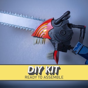 Puede incluir: Un kit de bricolaje listo para ensamblar que presenta una motosierra de utilería con una hoja plateada, una carcasa mecánica roja y negra y protuberancias blancas similares a dientes. El texto DIY KIT READY TO ASSEMBLE está impreso en negro sobre una banda amarilla.