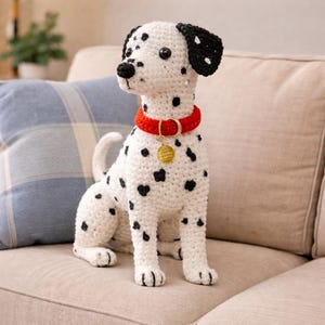 Peut inclure: Un chien dalmatien au crochet, avec des taches noires sur un corps blanc. Il a des oreilles noires, un nez noir et un collier rouge avec une étiquette dorée. Le chien est assis sur un canapé beige.