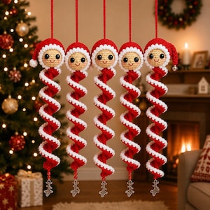 Peut inclure: Cinq décorations suspendues en crochet représentant une tête de poupée souriante avec un bonnet de Père Noël rouge et blanc. Chaque ornement possède un long corps en spirale rouge et blanc terminé par un petit charme renne en argent.