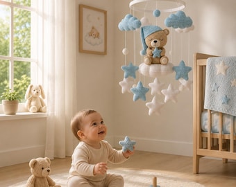 Pode incluir: Um móbile de berçário com um urso de crochê bege usando uma touca de dormir azul e segurando uma estrela azul, suspenso por um aro branco. O móbile inclui várias nuvens e estrelas de crochê brancas e azuis penduradas em fios brancos.