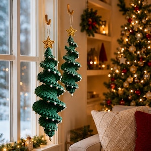 May include: Two spiral-shaped Christmas tree ornaments made of dark green crochet yarn. Each tree features small white beads along the edges and is topped with a yellow crocheted star. The ornaments hang from tan strings attached to wall hooks.
