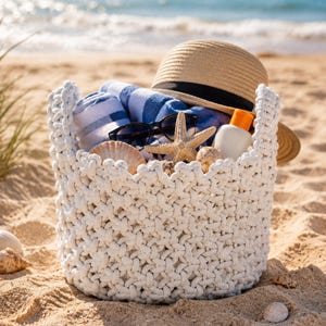 Peut inclure: Un panier blanc en crochet rempli d'articles de plage sur le sable. Il contient une serviette rayée bleue et blanche, des lunettes de soleil, un chapeau de paille, de la crème solaire, des coquillages et une étoile de mer. La mer est en arrière-plan.