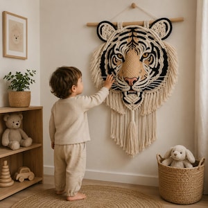 Peut inclure: Une décoration murale en macramé en forme de tête de tigre, composée de cordes nouées de couleur crème, noire et beige. Le motif présente des traits faciaux détaillés, des oreilles pointues et de longues franges suspendues à une tige en bois.