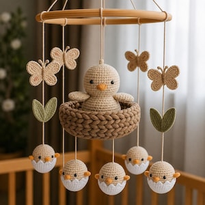 Peut inclure: Un mobile en crochet composé d'un poussin beige central dans un nid marron, entouré d'éléments suspendus incluant des papillons beiges, des feuilles vertes et des poussins sortant de coquilles d'œufs blanches, fixés à un anneau en bois.