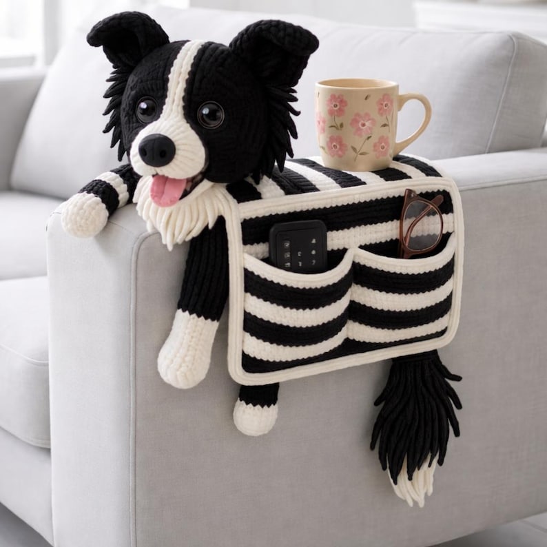 Puede incluir: Un organizador de reposabrazos de ganchillo con forma de border collie, cuerpo a rayas blancas y negras y dos bolsillos frontales. Incluye cabeza, patas y cola de perro de peluche, una taza beige con flores rosas y un mando a distancia.