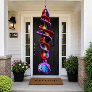 Peut inclure: Une décoration suspendue en spirale au crochet faite à la main, aux couleurs de l'arc-en-ciel, notamment rouge, orange, jaune, vert, bleu et violet. La spirale est suspendue devant une porte noire, ajoutant une touche de couleur.
