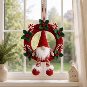 May include: A crocheted Christmas wreath featuring a central gnome with a red hat, white beard, and striped legs. The red circular wreath is decorated with green crocheted holly leaves, red berries, and red and white striped candy canes.