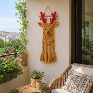 Peut inclure: Une décoration murale en macramé jaune moutarde en forme de tête de renne, dotée de bois recouverts de tissu rouge vif, d'un nez rouge et de trois longues franges à la base. L'ensemble est suspendu à une tige en bois avec une cordelette.