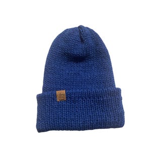 May include: A blue knitted beanie with a brown leather patch that says "Grew" on it.