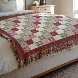 May include: A red, green and beige plaid throw blanket with fringe on the edges. The blanket is folded and draped over a bed.