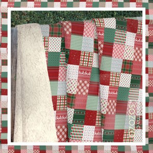K&ouml;nnte beinhalten: Eine Patchwork-Decke mit verschiedenen roten, gr&uuml;nen und wei&szlig;en Mustern. Die Decke besteht aus Quadraten und ist in der Mitte gefaltet. Die Decke liegt auf einem wei&szlig;en Kunstfell-&Uuml;berwurf.