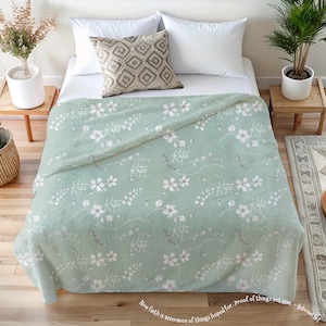 Könnte beinhalten: Eine weiche, grüne Fleece-Decke mit einem weißen Blumenmuster und dem Namen "Kate", der sich über die gesamte Oberfläche wiederholt. Die Decke ist in der Hälfte gefaltet und liegt auf einem Bett.