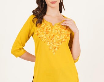Puede incluir: Túnica de color amarillo mostaza con mangas tres cuartos y cuello en V. La túnica presenta un intrincado bordado floral en tonos naranja y amarillo alrededor del escote. La prenda está hecha de una tela suave y tiene un ajuste relajado, adecuado para ropa casual.