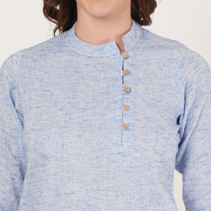 May include: A light blue linen shirt with a mandarin collar and a single button placket. The shirt has a subtle textured pattern.