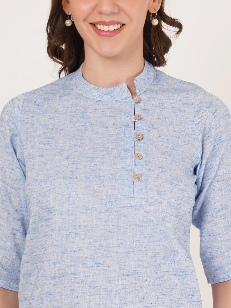 May include: A light blue linen shirt with a mandarin collar and a single button placket. The shirt has a subtle textured pattern.
