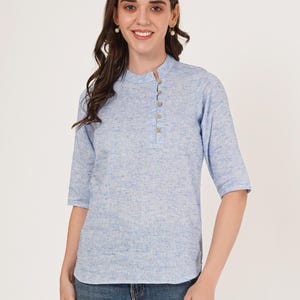 May include: A light blue linen shirt with a mandarin collar and a single button closure. The shirt has a textured, slightly speckled appearance.