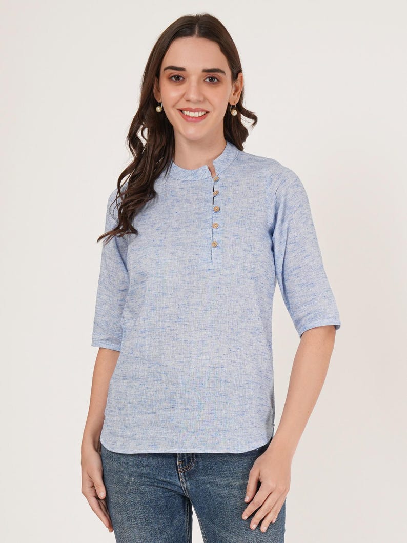 May include: A light blue linen shirt with a mandarin collar and a single button closure. The shirt has a textured, slightly speckled appearance.