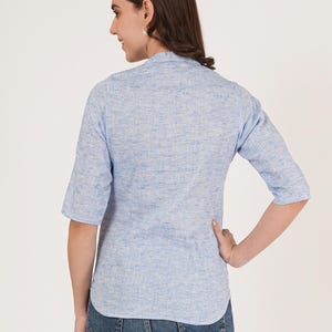 May include: A light blue linen shirt with a mandarin collar and three-quarter sleeves. The shirt is slightly fitted and has a textured look.
