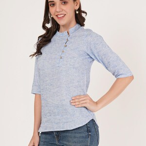 May include: A light blue linen top with a mandarin collar and three button closure. The top has a slightly fitted silhouette and three-quarter sleeves.