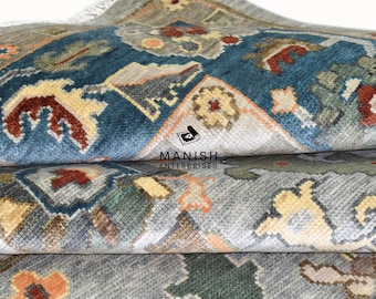 May include: Close-up of a folded rug with a blue, gray, and beige pattern. The rug has a traditional Persian design with intricate details. The rug is folded in thirds, revealing the different layers of the pattern.