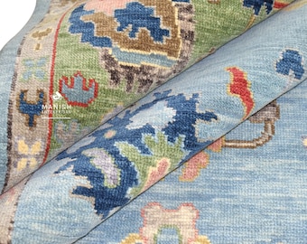 Könnte beinhalten: Ein blauer Teppich mit einem Muster aus geometrischen Formen und floralen Motiven in Blautönen, Grün, Rot und Gelb. Der Teppich hat einen Fransenrand.