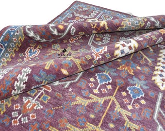 Op de afbeelding: Een vintage tapijt met een bordeauxrode achtergrond en ingewikkelde geometrische patronen in tinten blauw, geel en wit. Het tapijt is dubbelgevouwen, waardoor het gedetailleerde ontwerp wordt getoond.