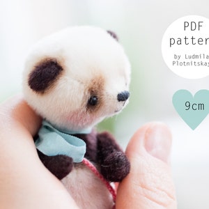 May include: A miniature panda bear plush toy with a white head, brown ears, and a blue scarf. The image includes text that says "PDF pattern" and "9cm". The panda is held in a person's hand.