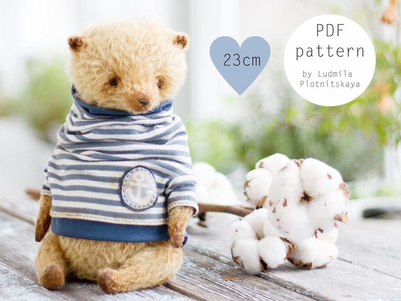 Op de afbeelding: Een PDF-patroon voor een 23 cm teddybeer die een blauw-wit gestreepte trui draagt met een ankerontwerp. Het patroon is van Ludmila Plotnitskaya.