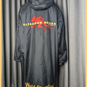 May include: Black hooded jacket with a red and yellow "ULTRAMAN HONDA" logo on the back. The jacket has a yellow "World Standard" logo on the bottom with the text "Modern Design Concepts" and the social media handle "@mustache_Jebron".
