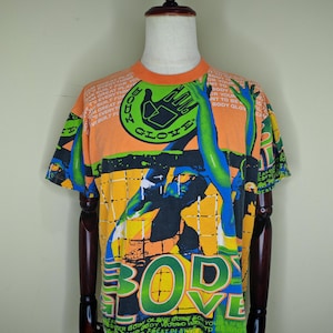 May include: Orange Body Glove t-shirt with a graphic design featuring a hand, the words "BODY GLOVE", and other text. The shirt has a crew neck and short sleeves. The design includes blue, green, and yellow accents.