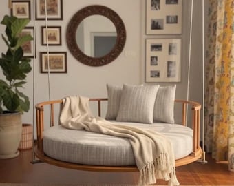 May include: A round, hanging daybed with a light gray cushion and wooden frame. Two matching pillows and a cream-colored throw blanket are on the daybed. The room has a rug, framed pictures, and a large mirror.