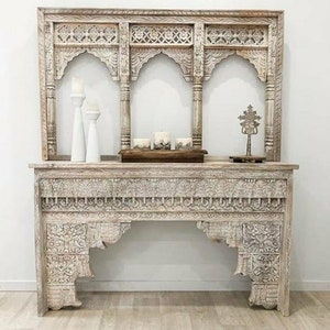 Puede incluir: Mesa consola de madera blanqueada con tallas intrincadas y un estante superior decorativo. La mesa tiene un diseño de arco tallado y es perfecta para un pasillo o una entrada.