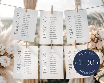 May include: Wedding seating chart with six table cards, each clipped to a string with wooden clothespins. The cards are white with black text, listing names and table numbers. A navy blue circle with the text "NUMBERS 1-30 INCLUDED" is also visible.
