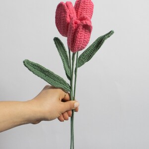 May include: A bouquet of three pink crocheted tulips with green crocheted stems and leaves.