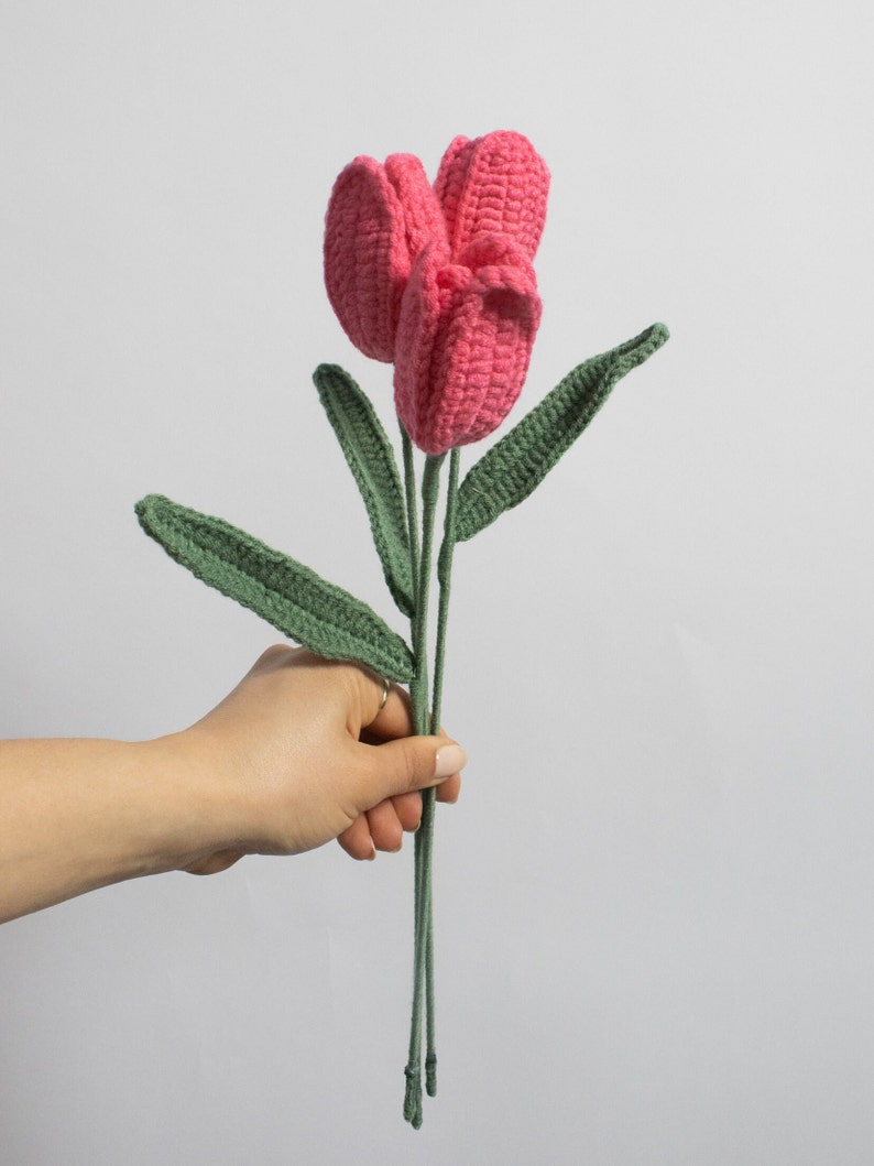 May include: A bouquet of three pink crocheted tulips with green crocheted stems and leaves.