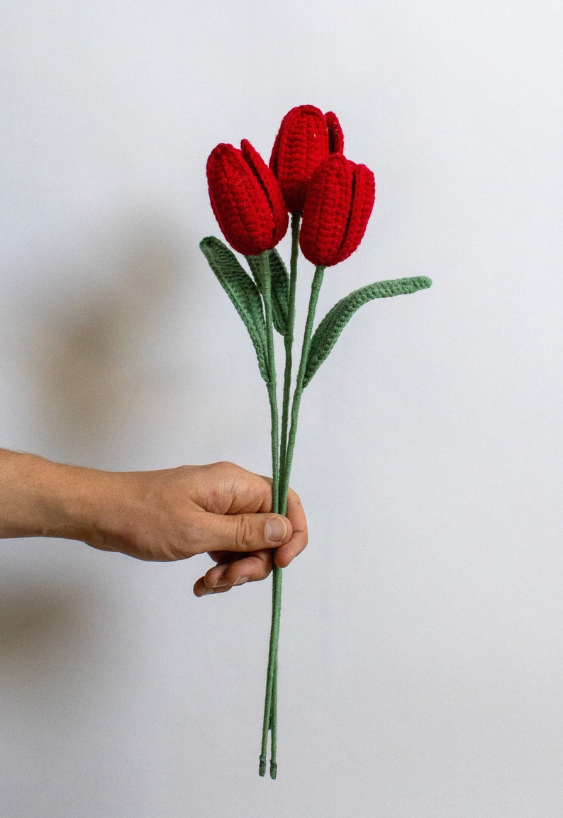 May include: A bouquet of three red crocheted tulips with green stems and leaves.