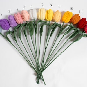 May include: A set of 13 crocheted tulips in various colors, including light blue, purple, pink, white, yellow, orange, red, and pink. The tulips are arranged in a fan shape with their stems bundled together.