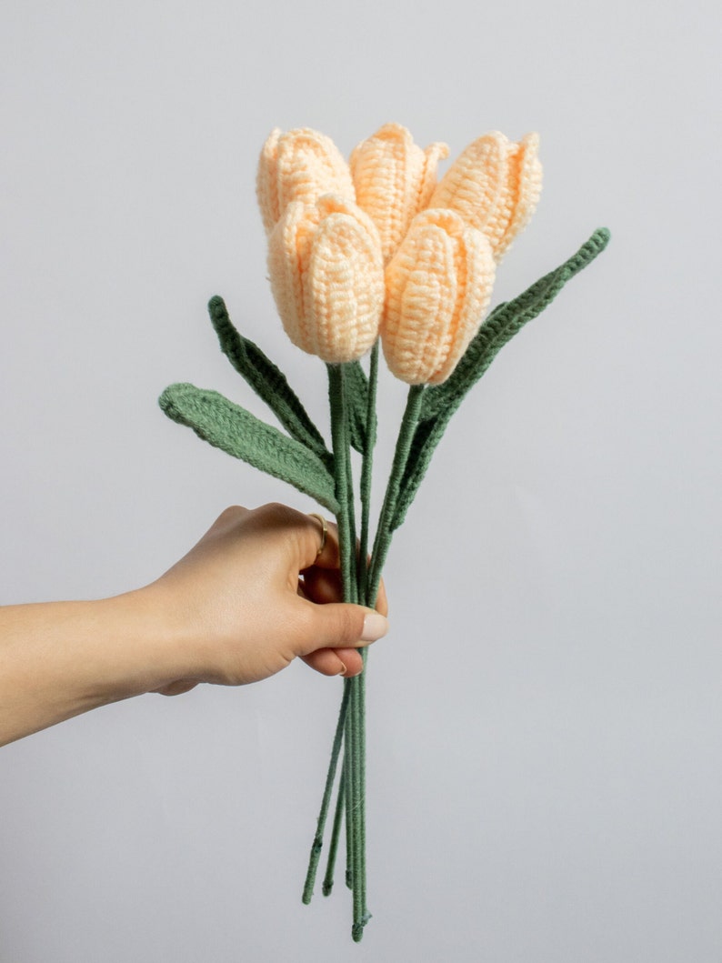 May include: A bouquet of five crocheted peach-colored tulips with green stems and leaves.