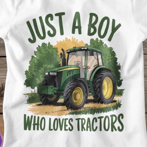 May include: White t-shirt featuring a green tractor graphic with yellow wheels. The text "JUST A BOY WHO LOVES TRACTORS" is printed above and below the tractor illustration in green. The shirt is made of a soft material.