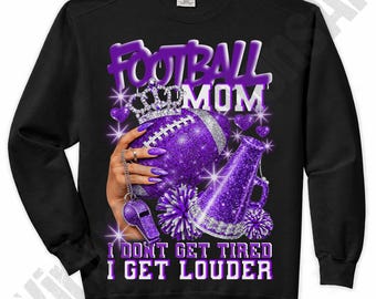 May include: Black sweatshirt with a purple graphic that says "FOOTBALL MOM". The graphic includes a football, crown, megaphone, and pom-poms. The text "I DON'T GET TIRED I GET LOUDER" is also included.