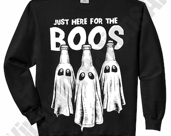 May include: A black long-sleeve sweatshirt featuring a white graphic of three glass bottles draped in white sheets to resemble ghosts. Above the bottles, the text reads JUST HERE FOR THE BOOS in a bold, white, sans-serif font style.
