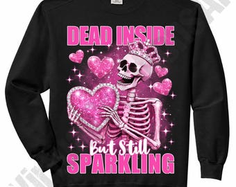 May include: Black sweatshirt with a pink skeleton graphic holding a sparkling heart and wearing a crown. The text "DEAD INSIDE" and "But Still SPARKLING" are in pink. Pink hearts and stars complete the design.